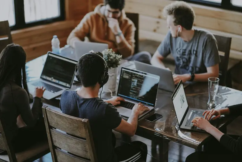 Personas colaborando alrededor de una mesa de trabajo con computadores portátiles