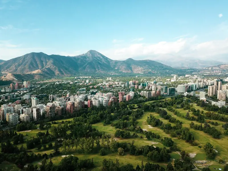 Vista aérea de Santiago con edificios, áreas verdes y la cordillera de fondo en un día despejado